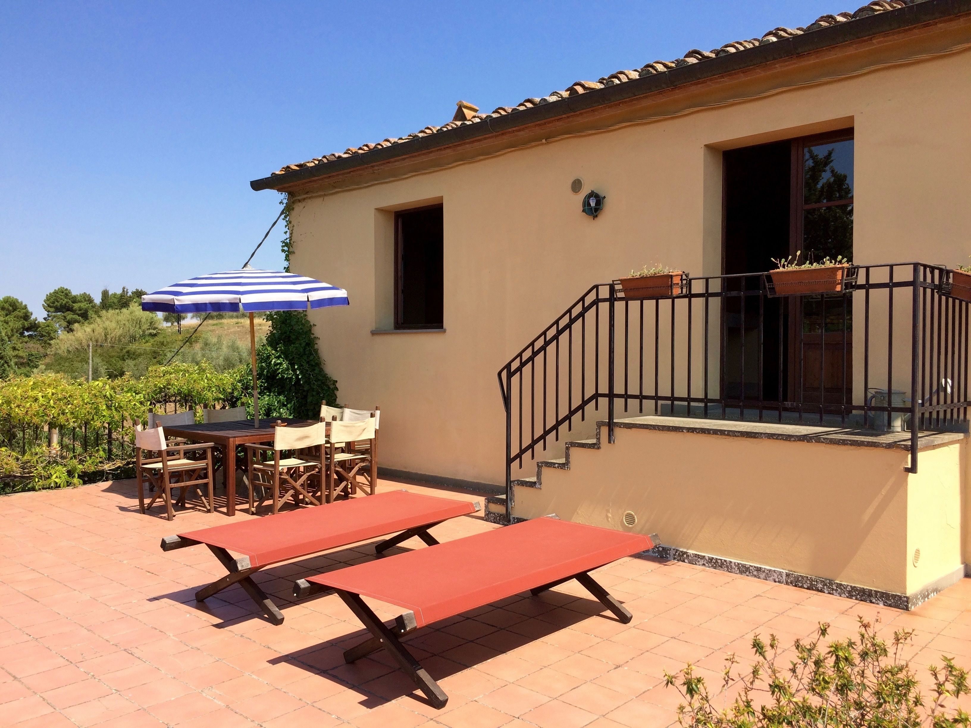 Un patio con una mesa, sillas, un paraguas azul y blanco a rayas y un banco rojo.