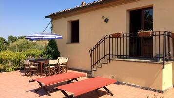 Un patio con una mesa, sillas, un paraguas azul y blanco a rayas y un banco rojo.