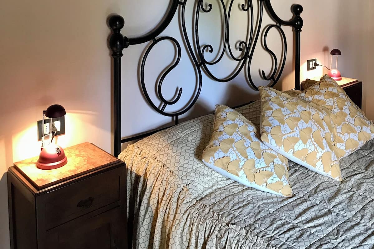 A bedroom with a metal bed frame, a bedside table with a lamp, and a painting on the wall.