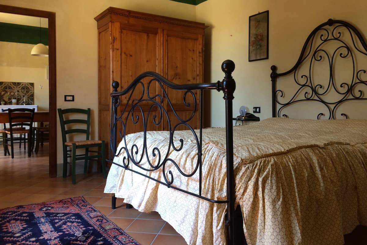 A bedroom with a bed, wooden wardrobe, and a dining area with chairs and a table.