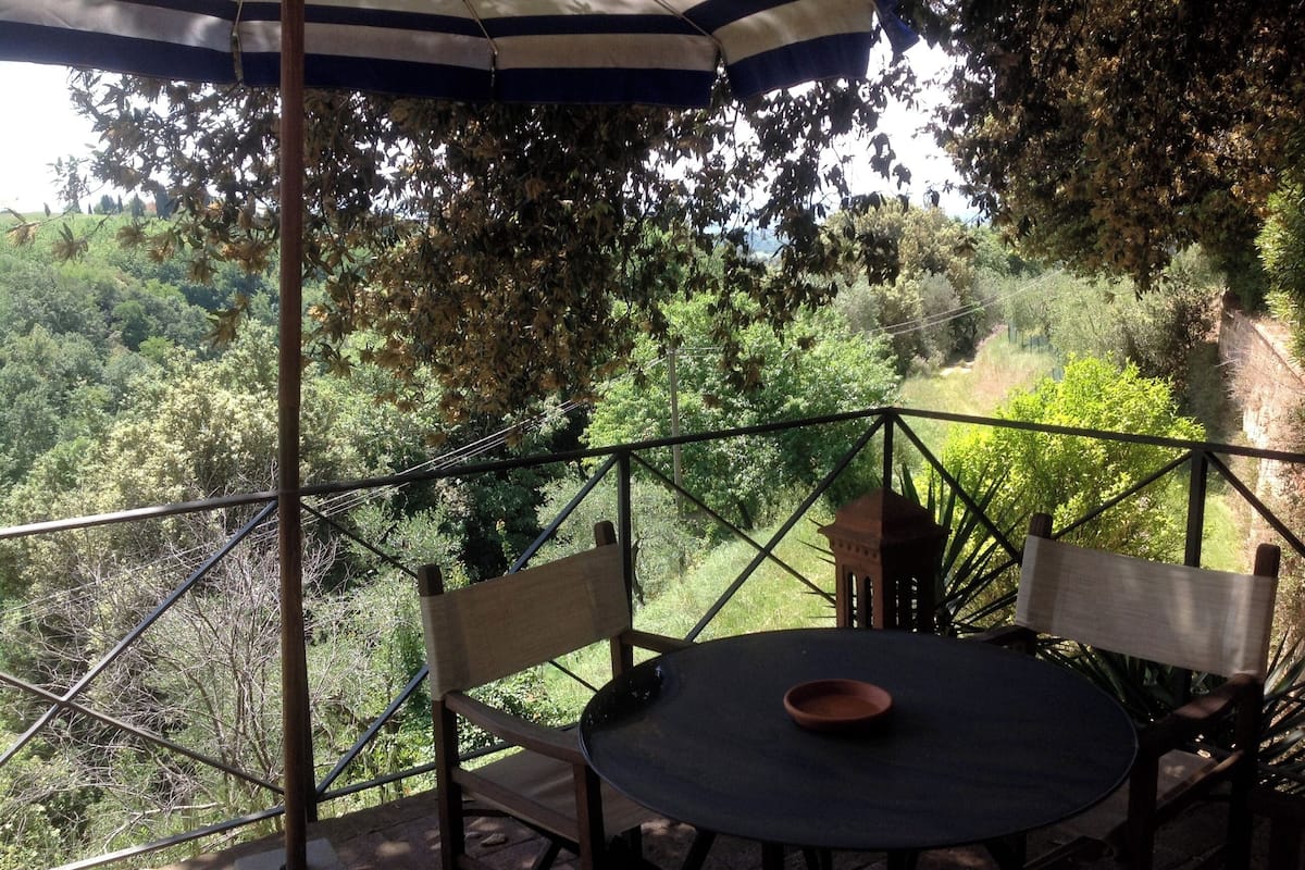 An outdoor patio with a round table and chairs, surrounded by a metal railing, overlooking a lush green landscape.