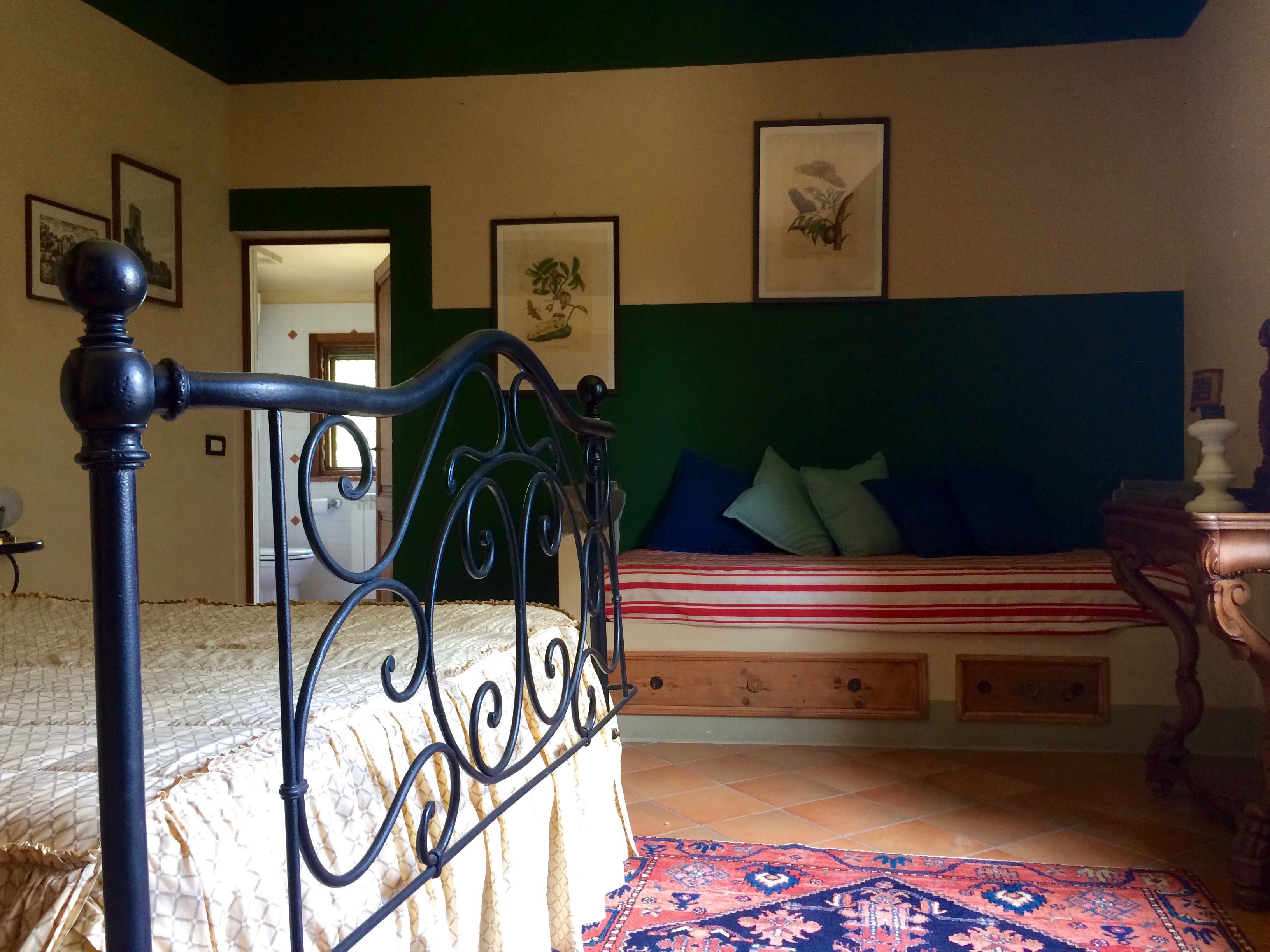 Een slaapkamer met een bed, een houten nachtkastje, een kamerkleed met patroon en lijstwerken aan de muren.
