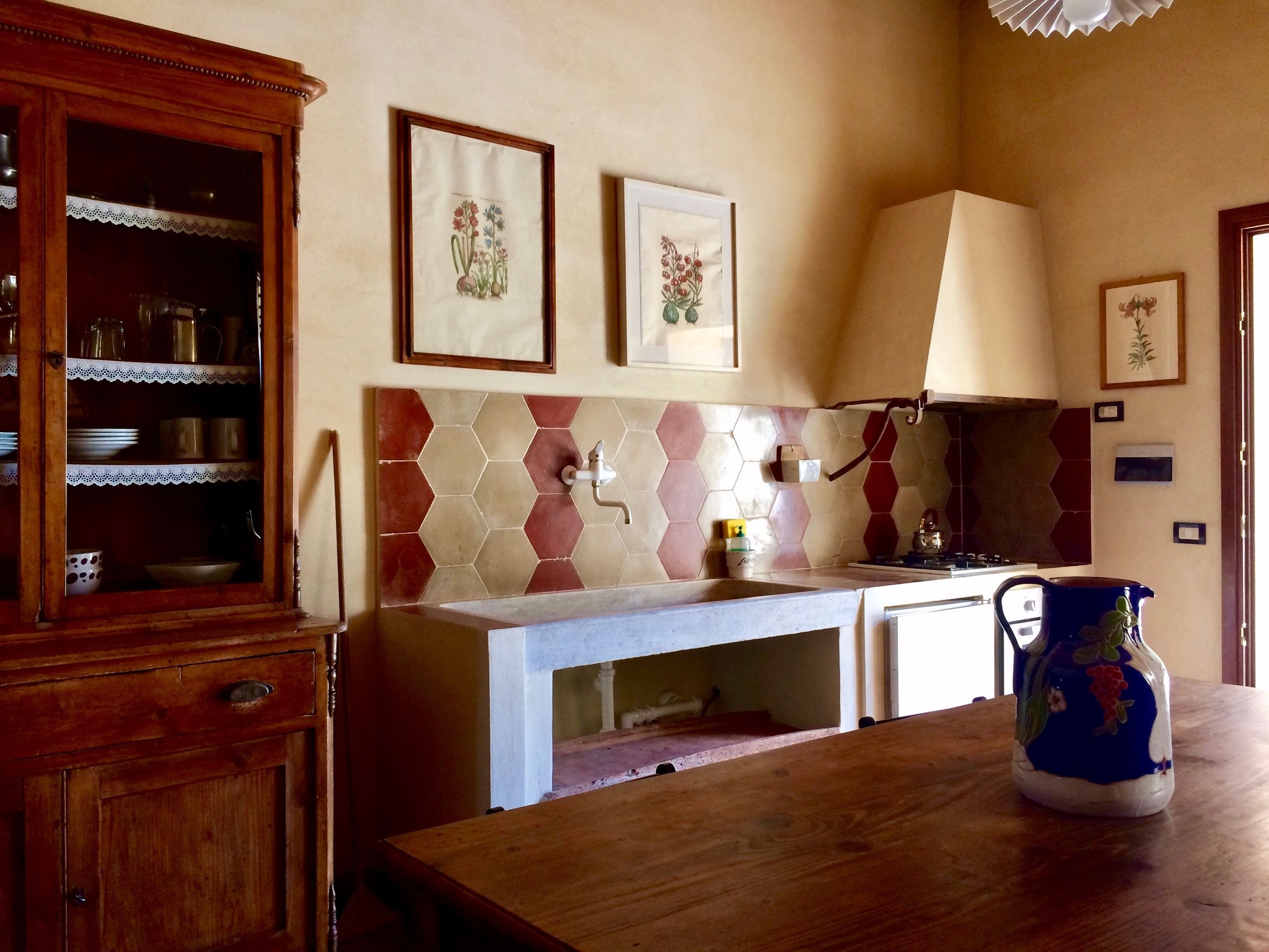 Una cocina con un mueble de madera, salpicadero de azulejos y una jarra azul sobre la encimera.