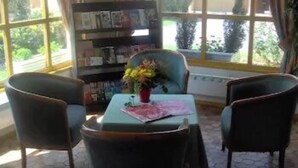 Een kamer met een groot raam, een boekenkast, een tafel met een bloevas en twee stoelen.