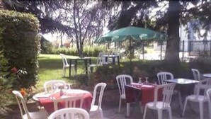 Een terras buiten met witte plastic stoelen en tafels, waarvan sommige onder parasols staan, en een stenen vloer.