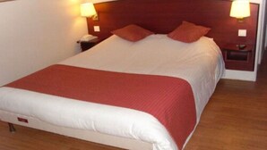 Een net opgemaakt bed met een rode en witte sprei, twee rode kussens en twee bedlampjes op houten nachtkastjes.