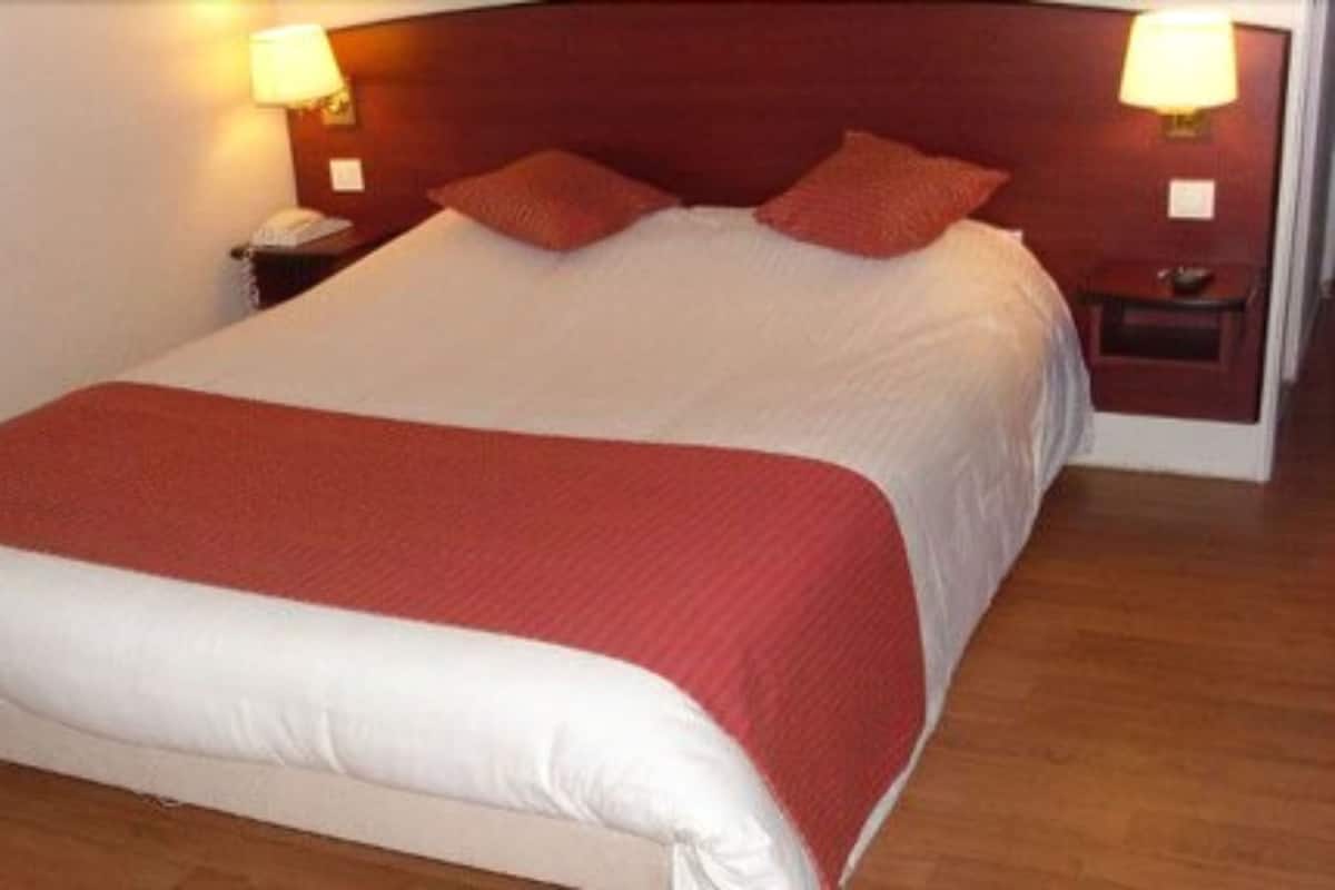 A neatly made bed with a red and white bedspread, two red pillows, and two bedside lamps on wooden nightstands.