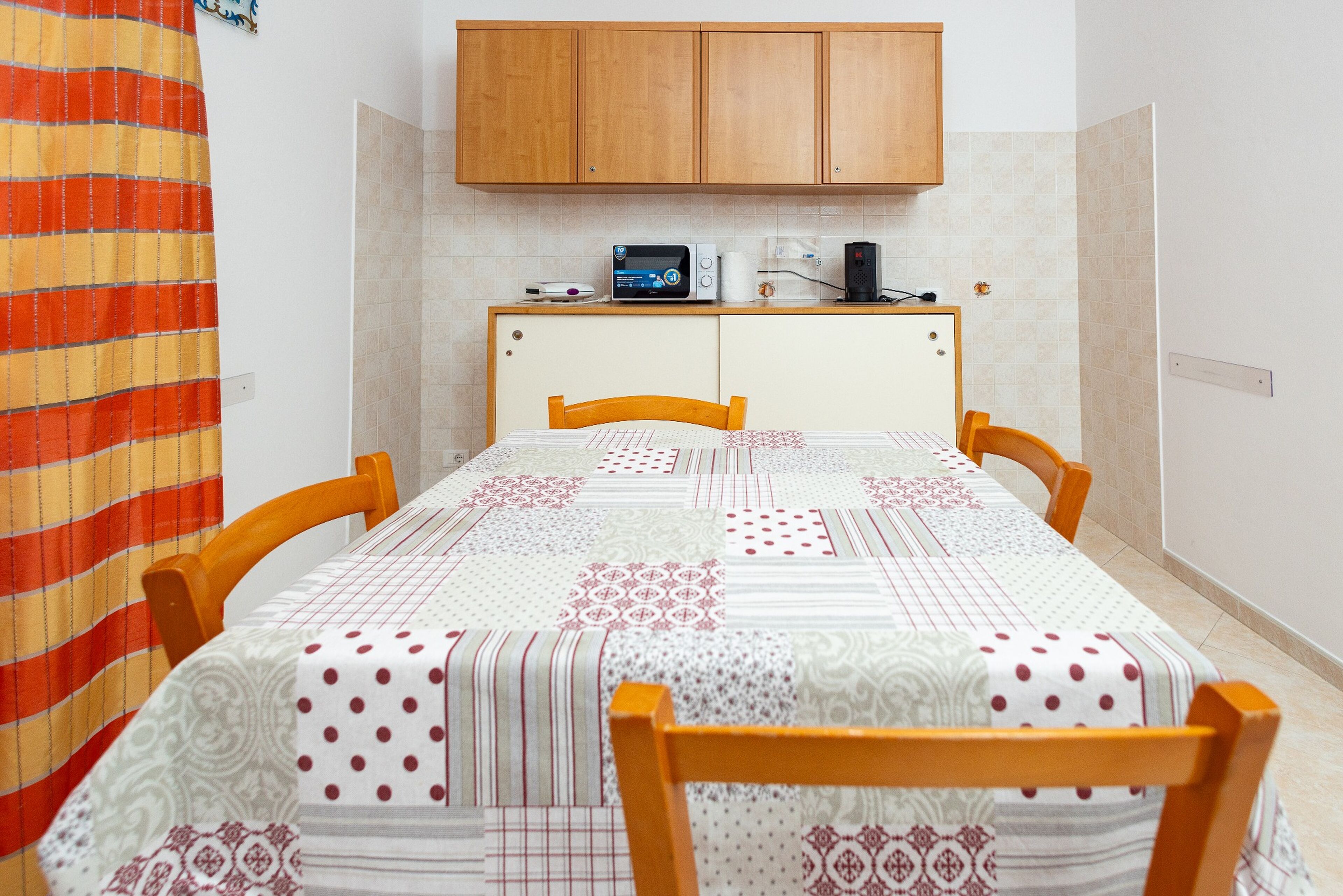 Un comedor con una mesa dispuesta para cuatro, un mueble de madera arriba y una cortina a rayas a la izquierda.