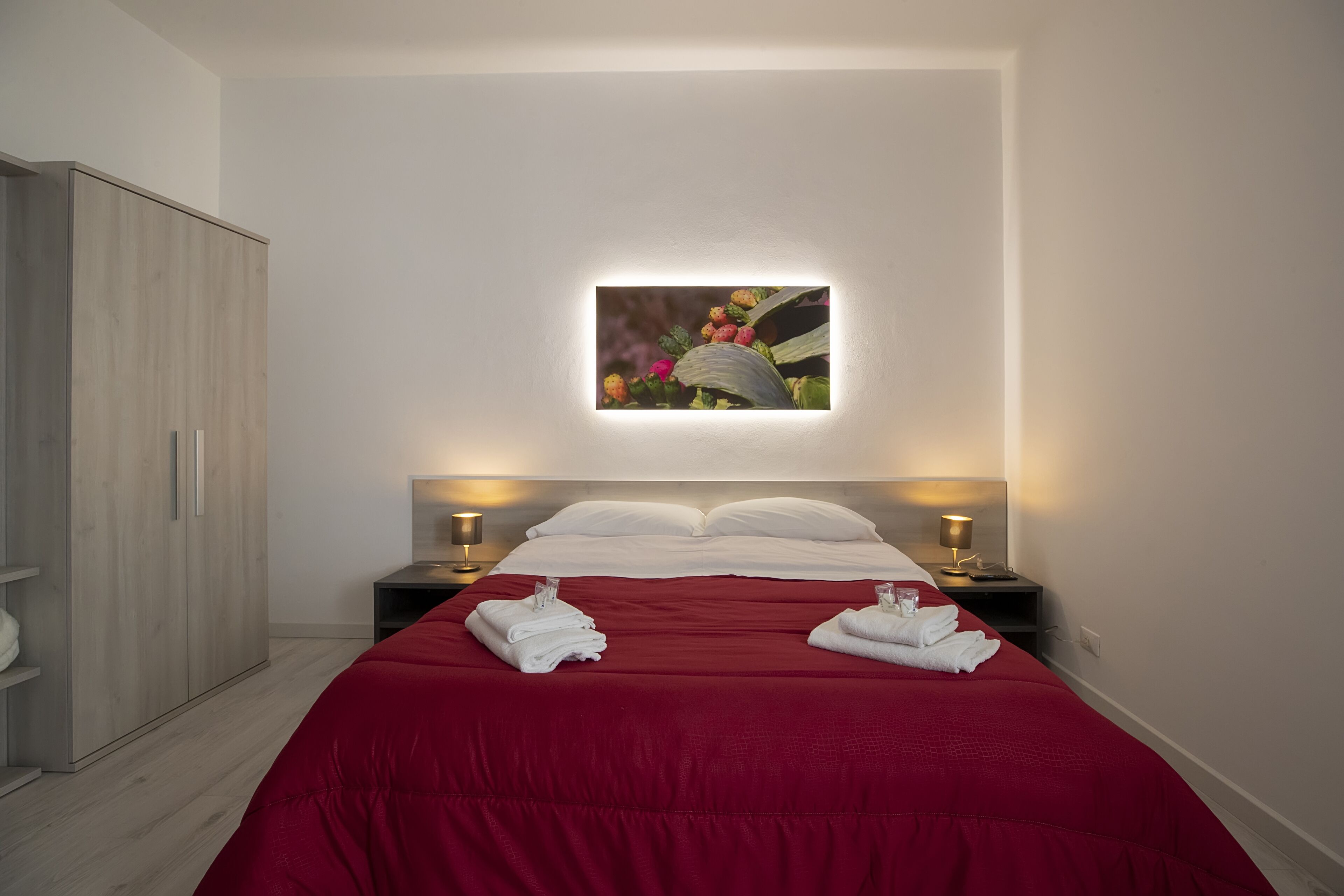 A hotel room with a bed, two bedside tables with lamps, a wardrobe, and a framed picture on the wall.
