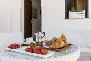 A breakfast setup with strawberries, a croissant, and a coffee pot on a wicker table.