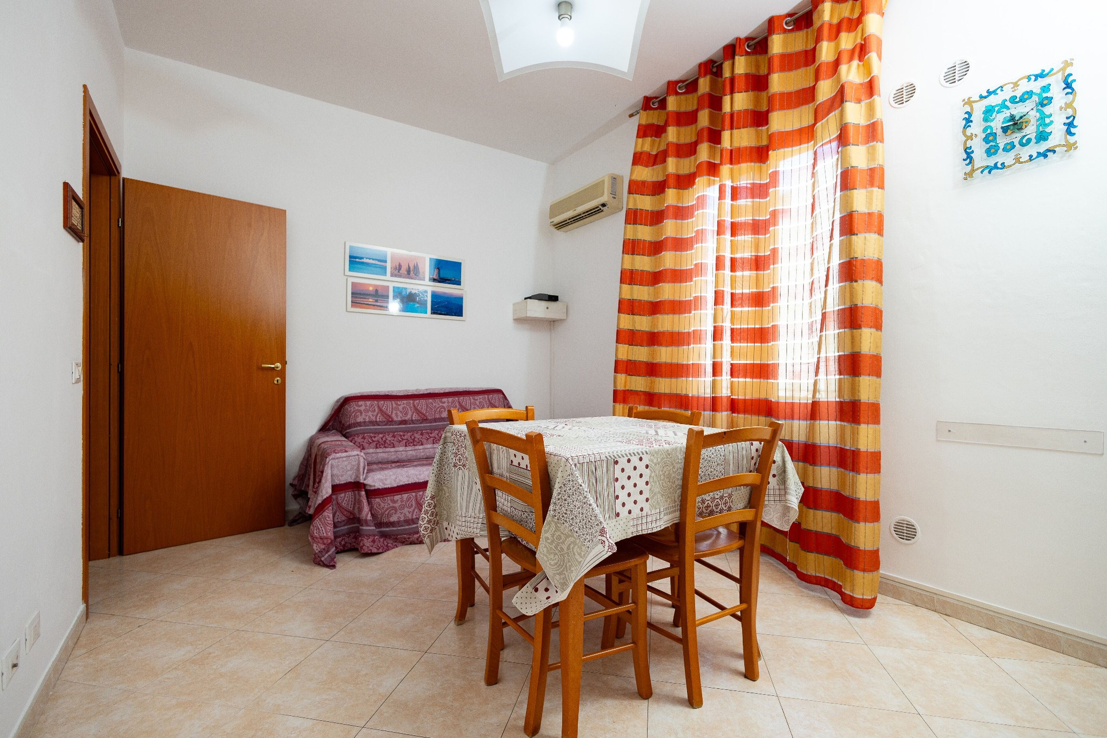 Una zona pranzo modesta con tavolo e sedie, un divano, una porta e una finestra con tende.