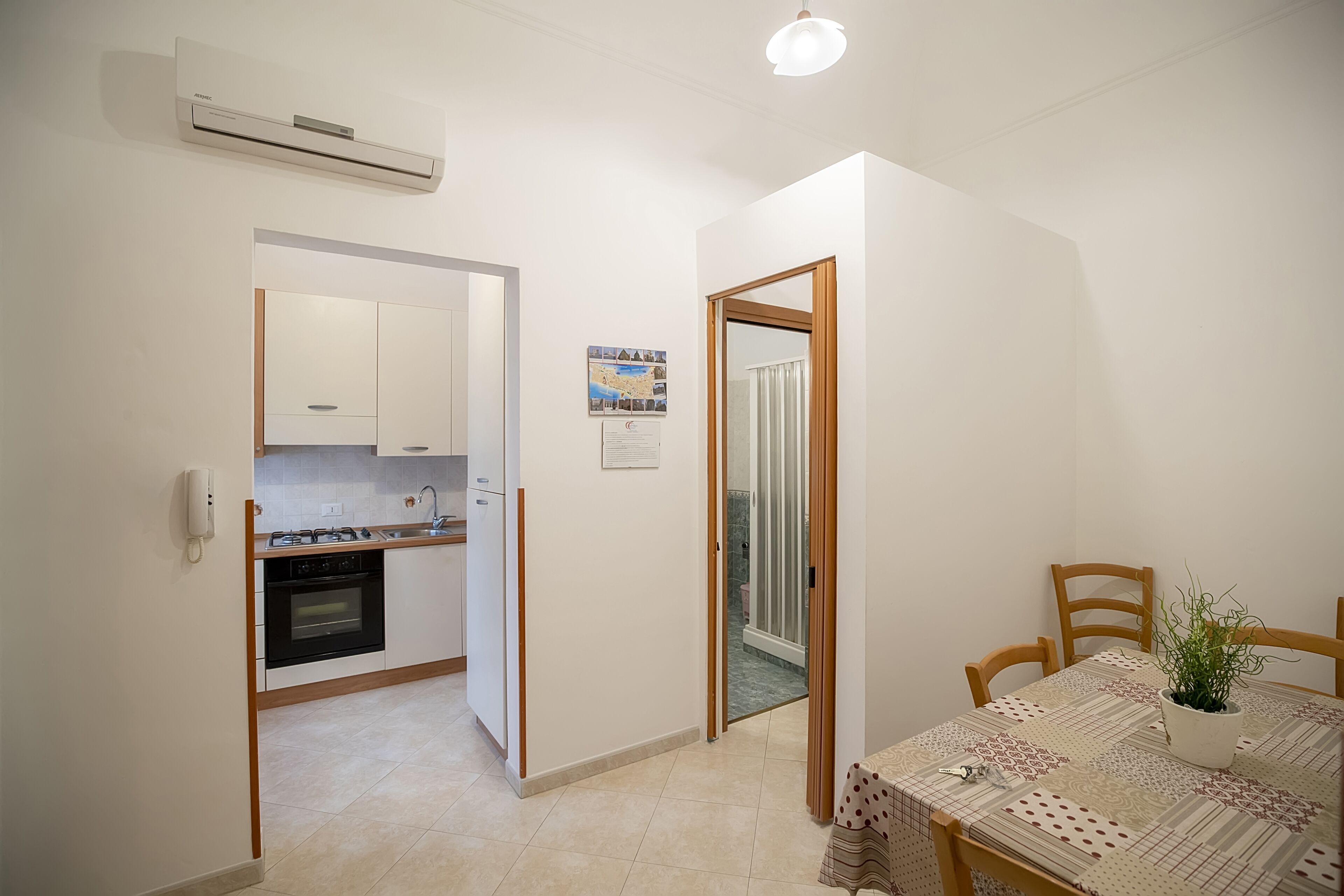 Una cocina compacta con armarios blancos, horno integrado y un pequeño comedor con mesa y sillas.