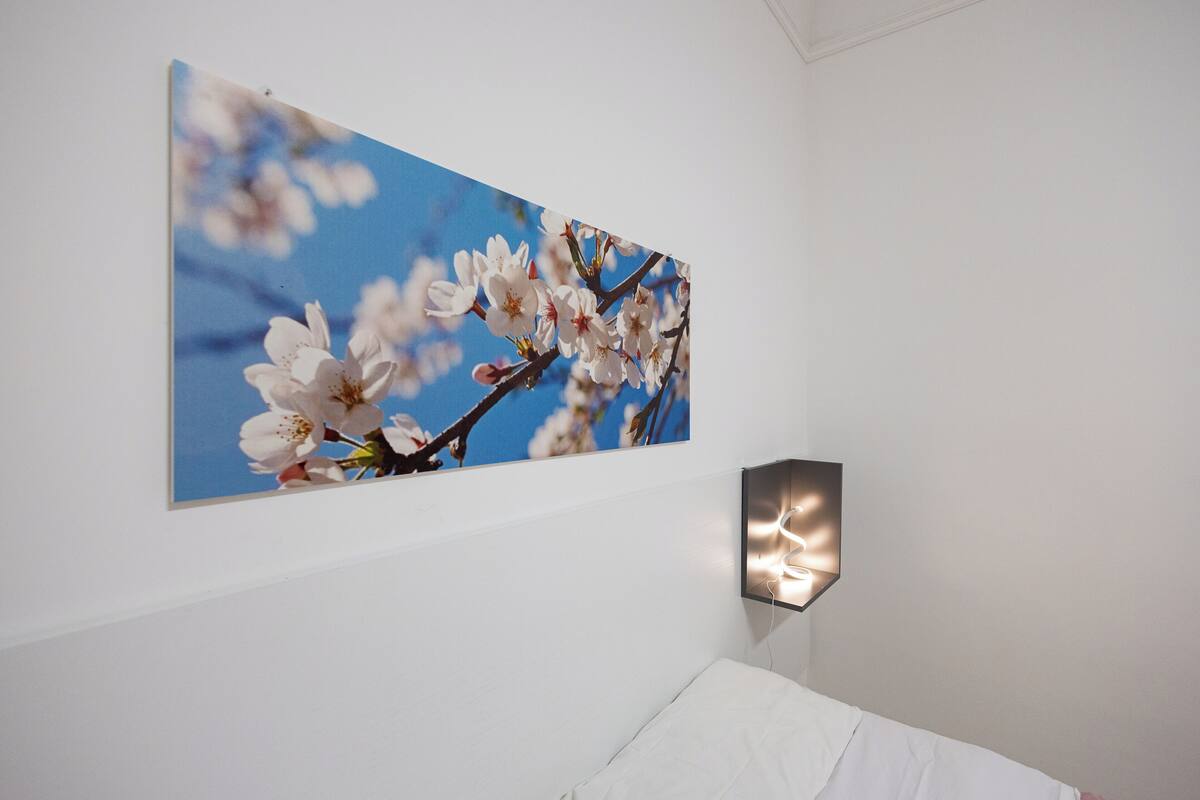 Un dormitorio con un ventanal grande, una cama y una lámpara fijada a la pared.