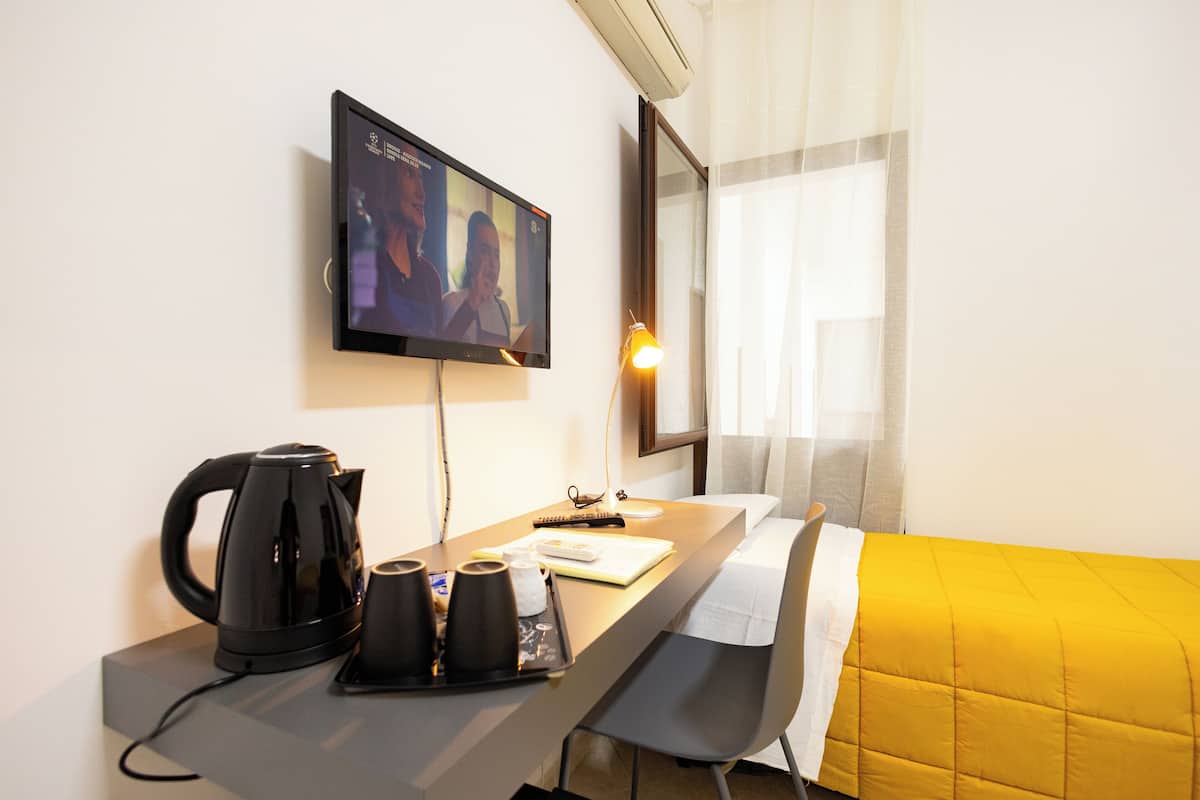 Una habitación de hotel con cama, escritorio con cafetera, televisión y ventana con cortinas.