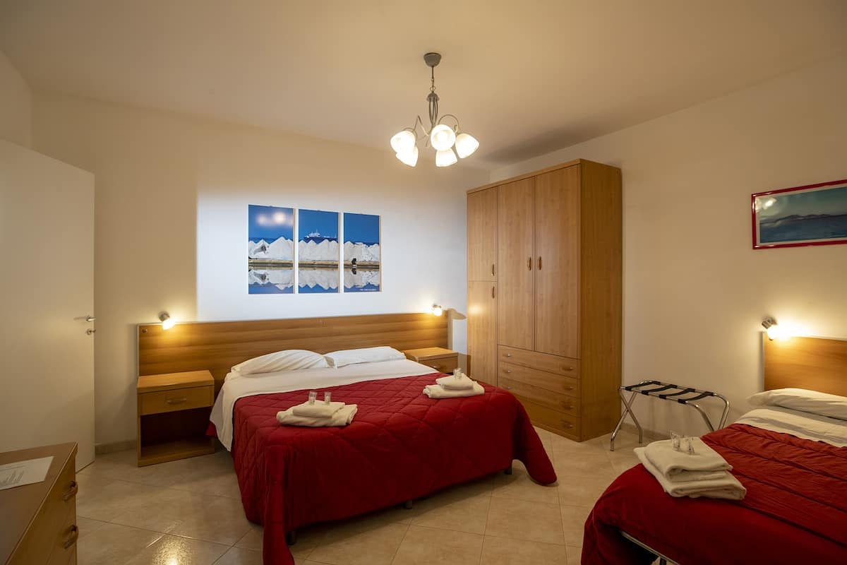 Una habitación de hotel con dos camas, un armario de madera, un cuadro colgado en la pared y una lámpara en el techo.