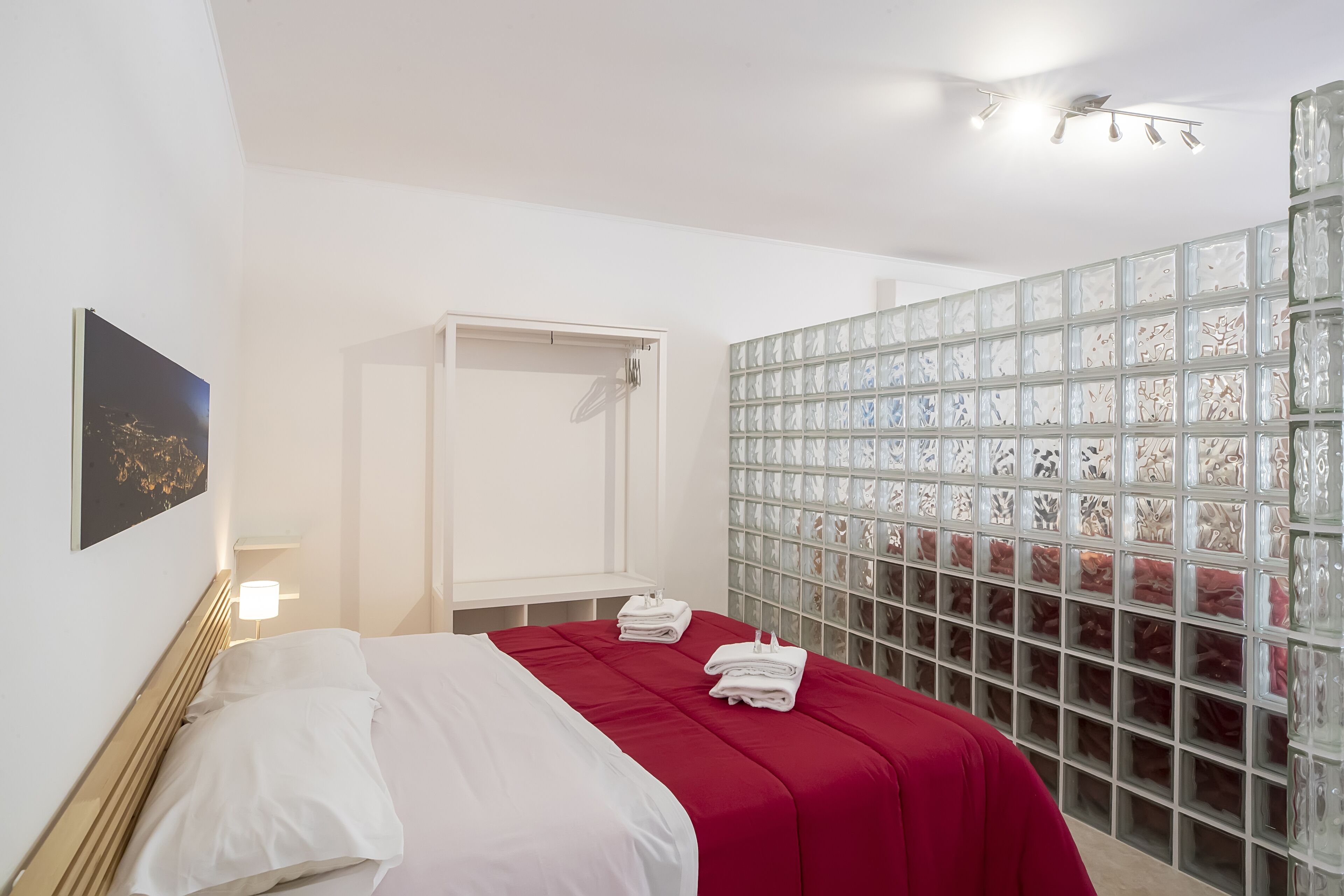 Camera d'albergo con un letto, un armadio, un muro in vetro blocchetto e una luce a soffitto.