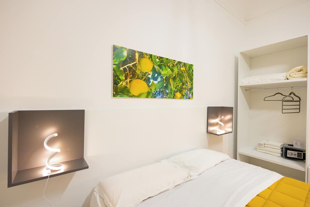 Un dormitorio con cama, una obra de arte en la pared y un estante con toallas y un radio.