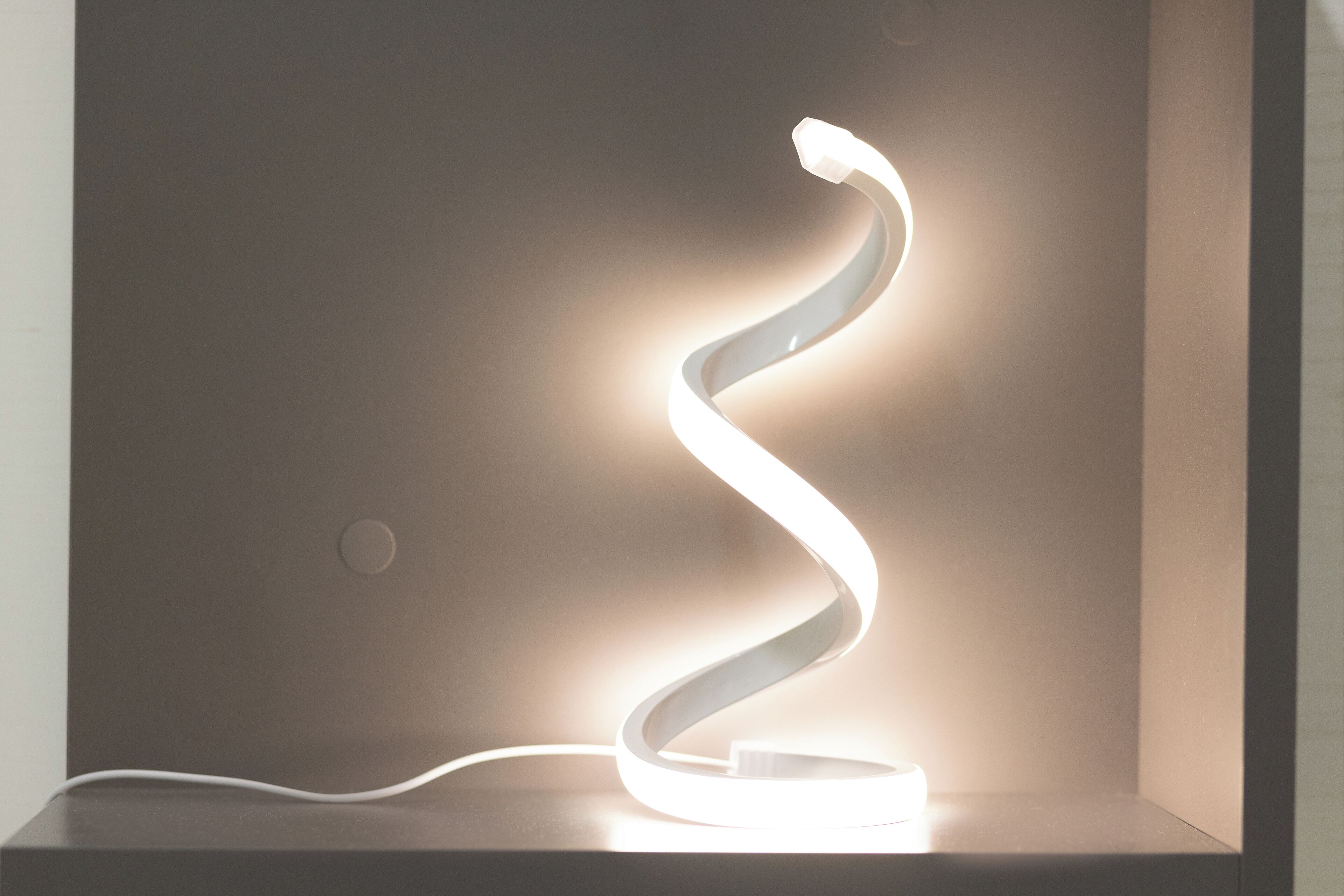A modern, minimalist light fixture with a curved design, mounted on a white pedestal.