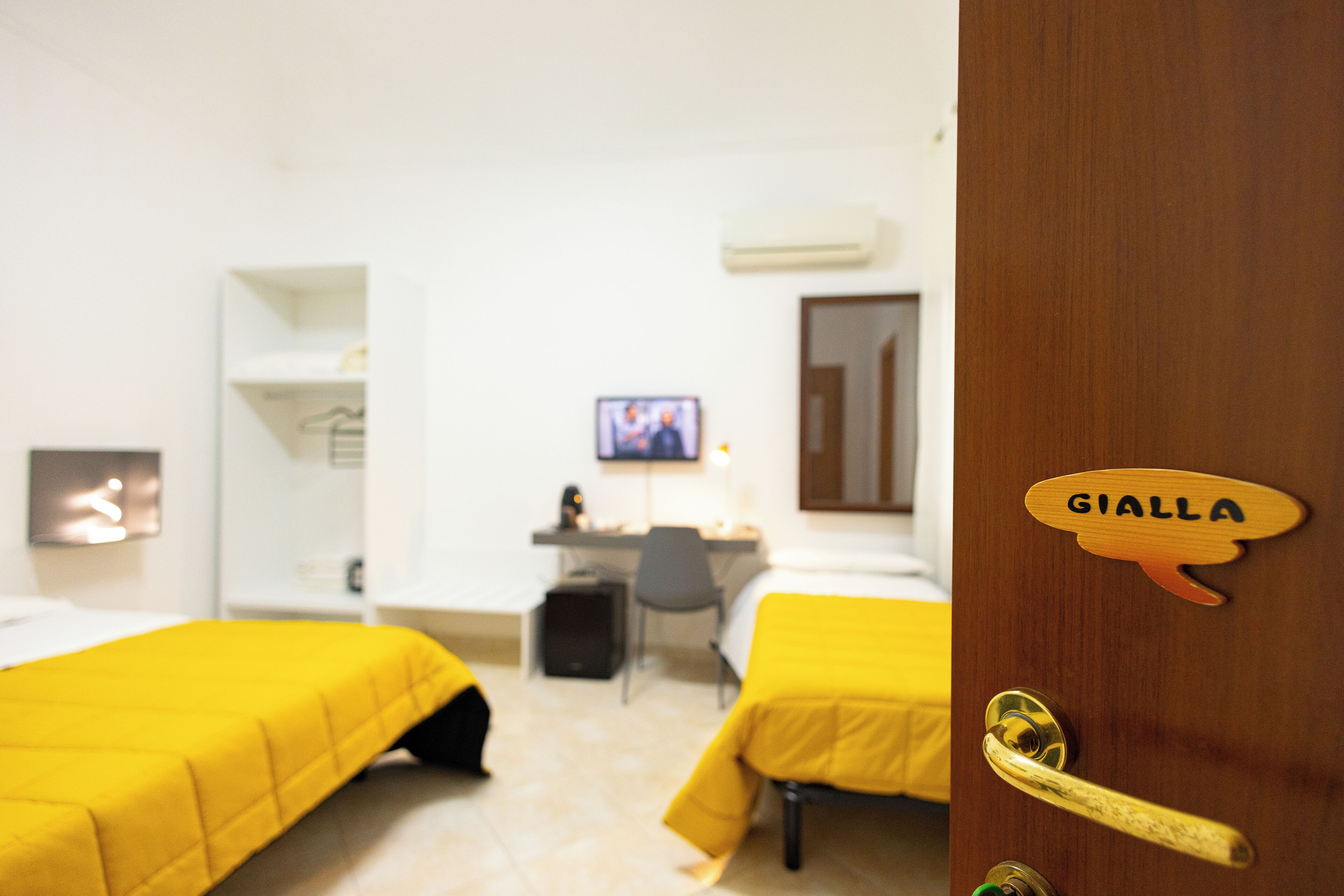 Une chambre d’hôtel avec deux lits, un bureau, une chaise, un téléviseur et une porte avec une plaque nominative.