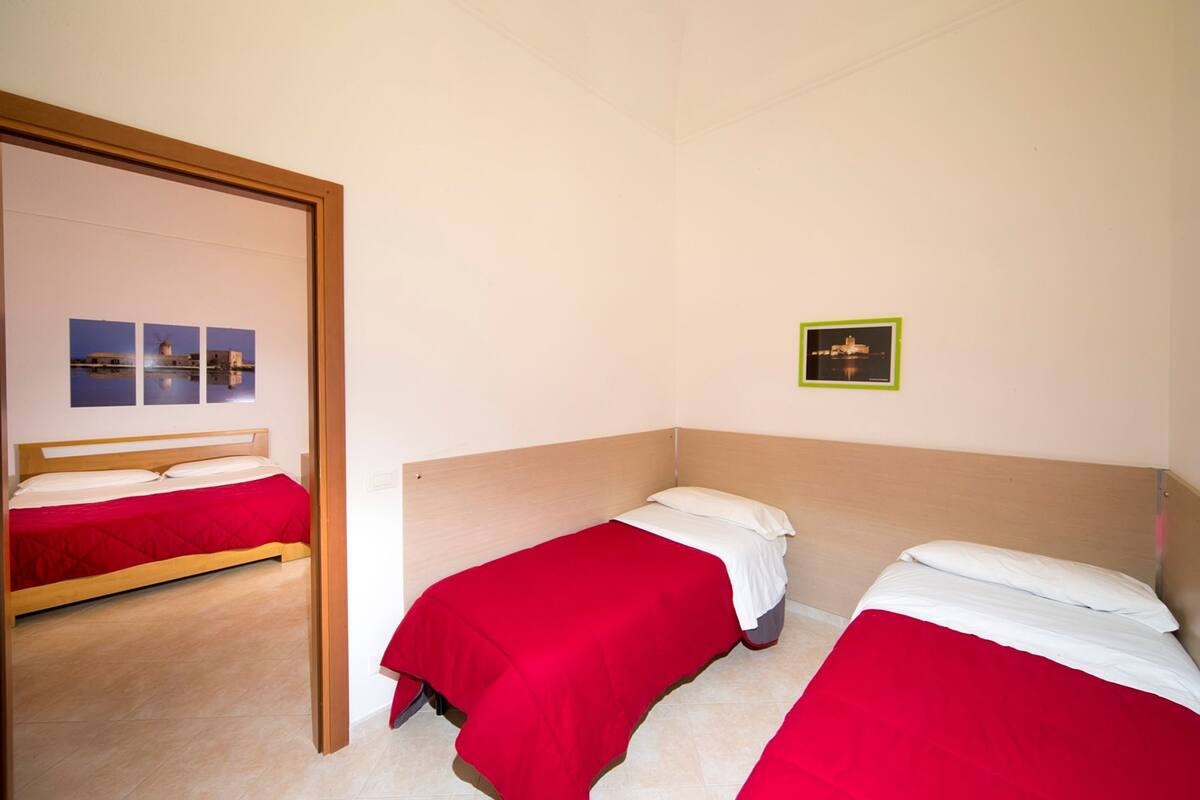 Habitación de hotel con dos camas individuales, cada una con una colcha roja y almohadas blancas. Encima de las camas hay un cuadro en la pared.