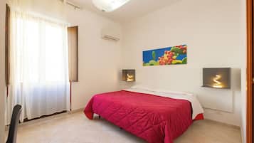 A bedroom with a bed, a window with curtains, an air conditioner, and a wall-mounted light fixture.