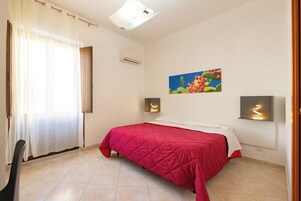 A bedroom with a bed, a window with curtains, an air conditioner, and a wall-mounted light fixture.