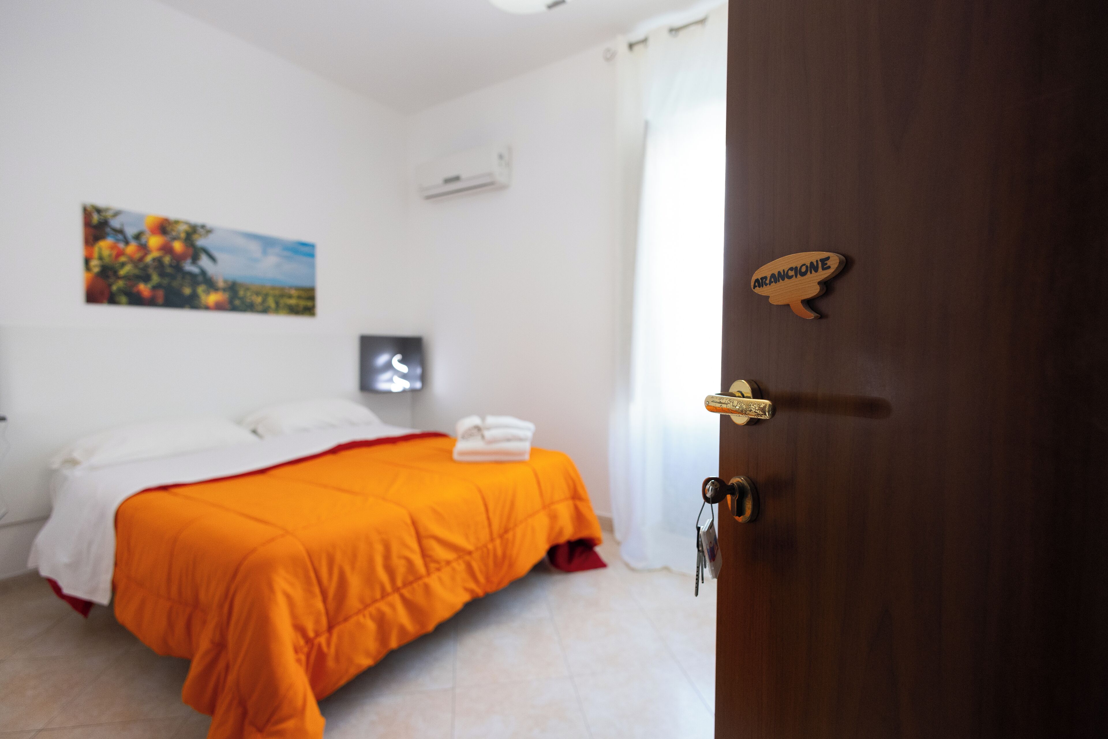 A bedroom with a bed, a painting, an air conditioner, and a wooden door with a sign.