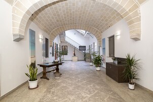 A spacious hallway with a high ceiling, a staircase, and potted plants.