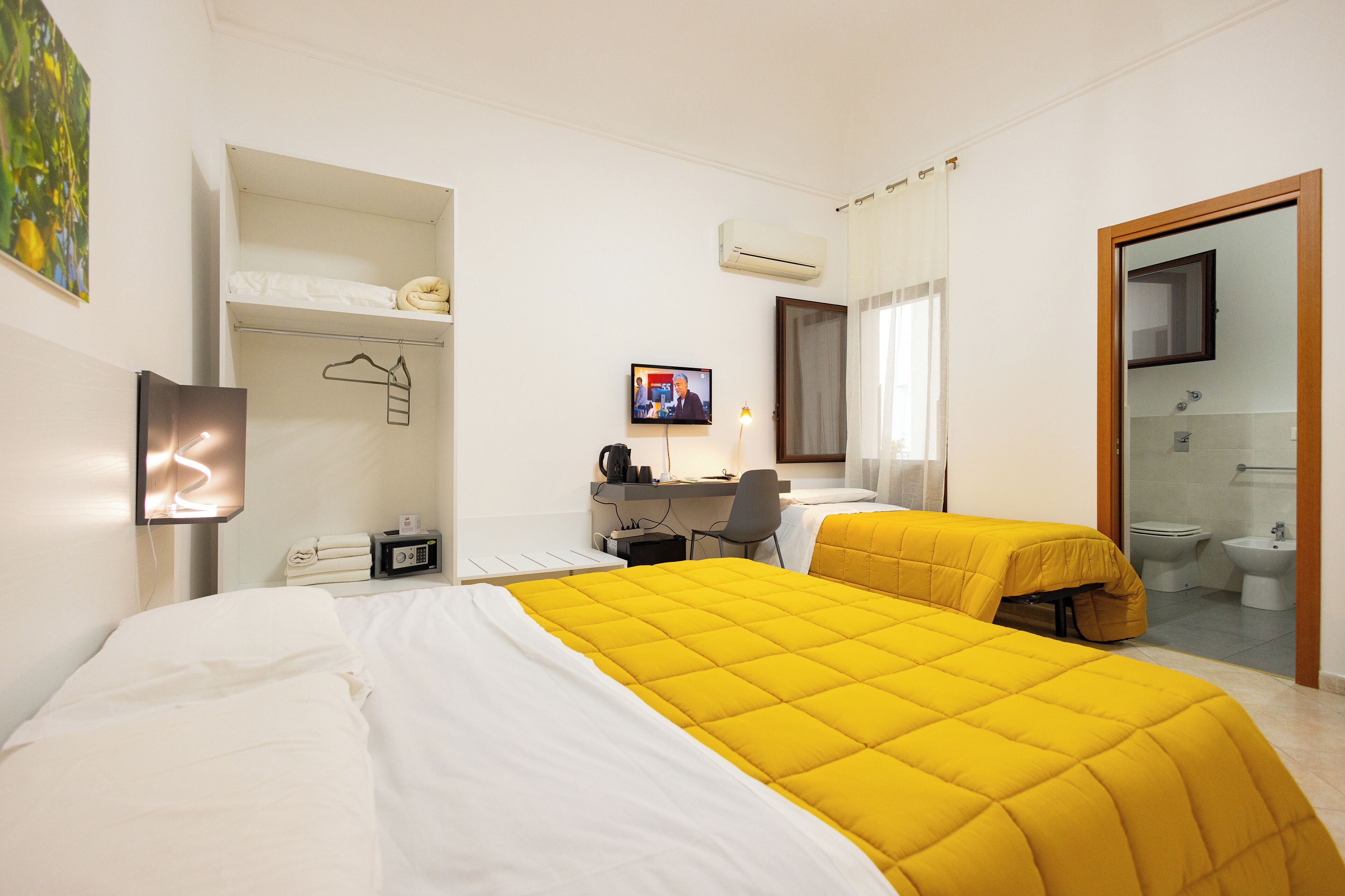 A hotel room with a bed, a desk, a chair, a TV, and a bathroom visible through an open door.
