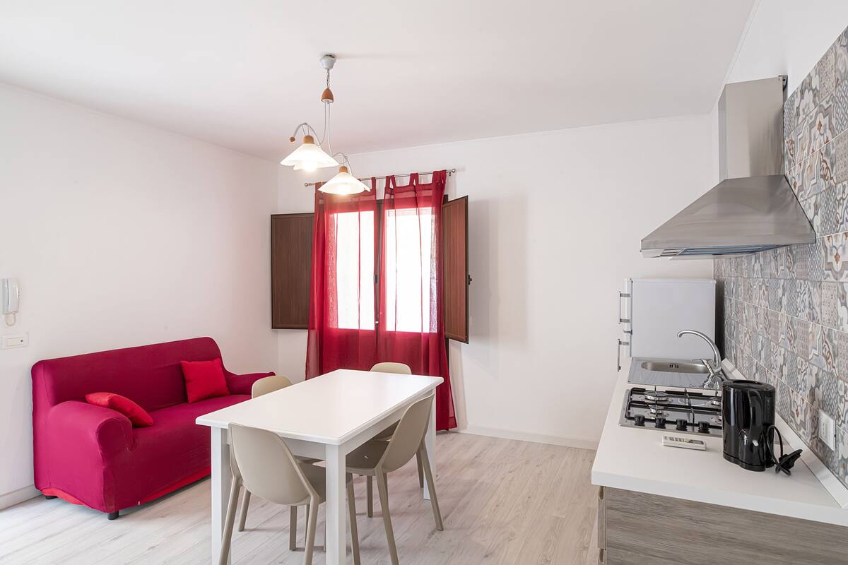 Un espacio habitable compacto con un sofá rojo, una mesa de comedor blanca y una kitchenette.