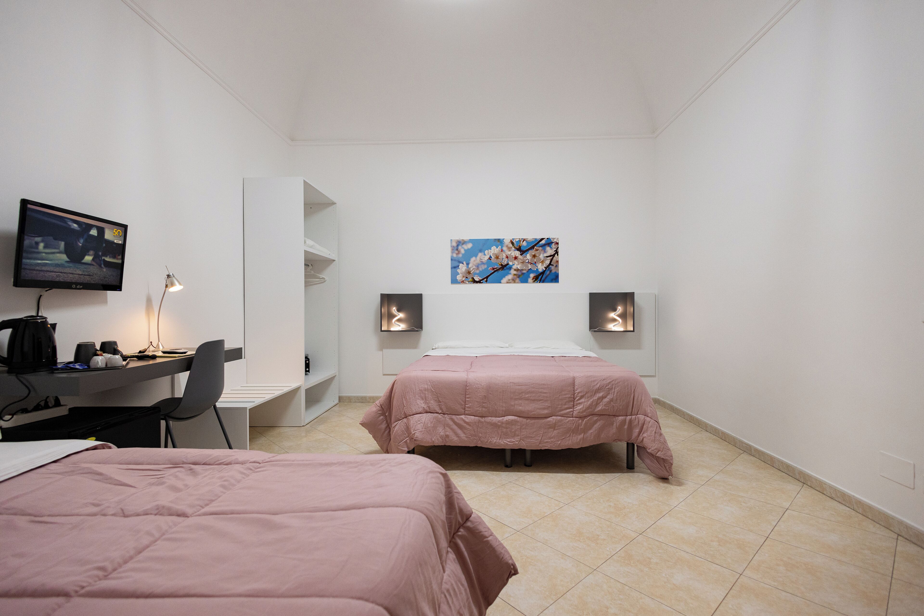 Habitación de hotel con dos camas, un escritorio con silla, televisión y un cuadro en la pared.