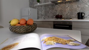 A kitchen with a woven basket of fruits, a cookbook open to a pasta recipe, and a modern stove. - CasaTrapani (Trapani)