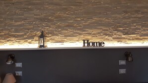 A room with a stone wall, a window with the word "Home" illuminated, a lantern, and wall-mounted light fixtures. - La Locanda dell'Angelo (Rome)