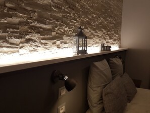 A room with a textured wall, a small table with a lantern, a bed with pillows, and a wall-mounted lamp. - La Locanda dell'Angelo (Rome)