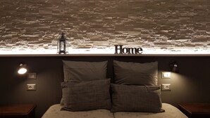 A bedroom with a stone wall, a bed with two pillows, and a 'Home' sign above the bed. - La Locanda dell'Angelo (Rome)