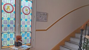 Una escalera con barandilla, una silla de mimbre con revistas y un felpudo con texto.