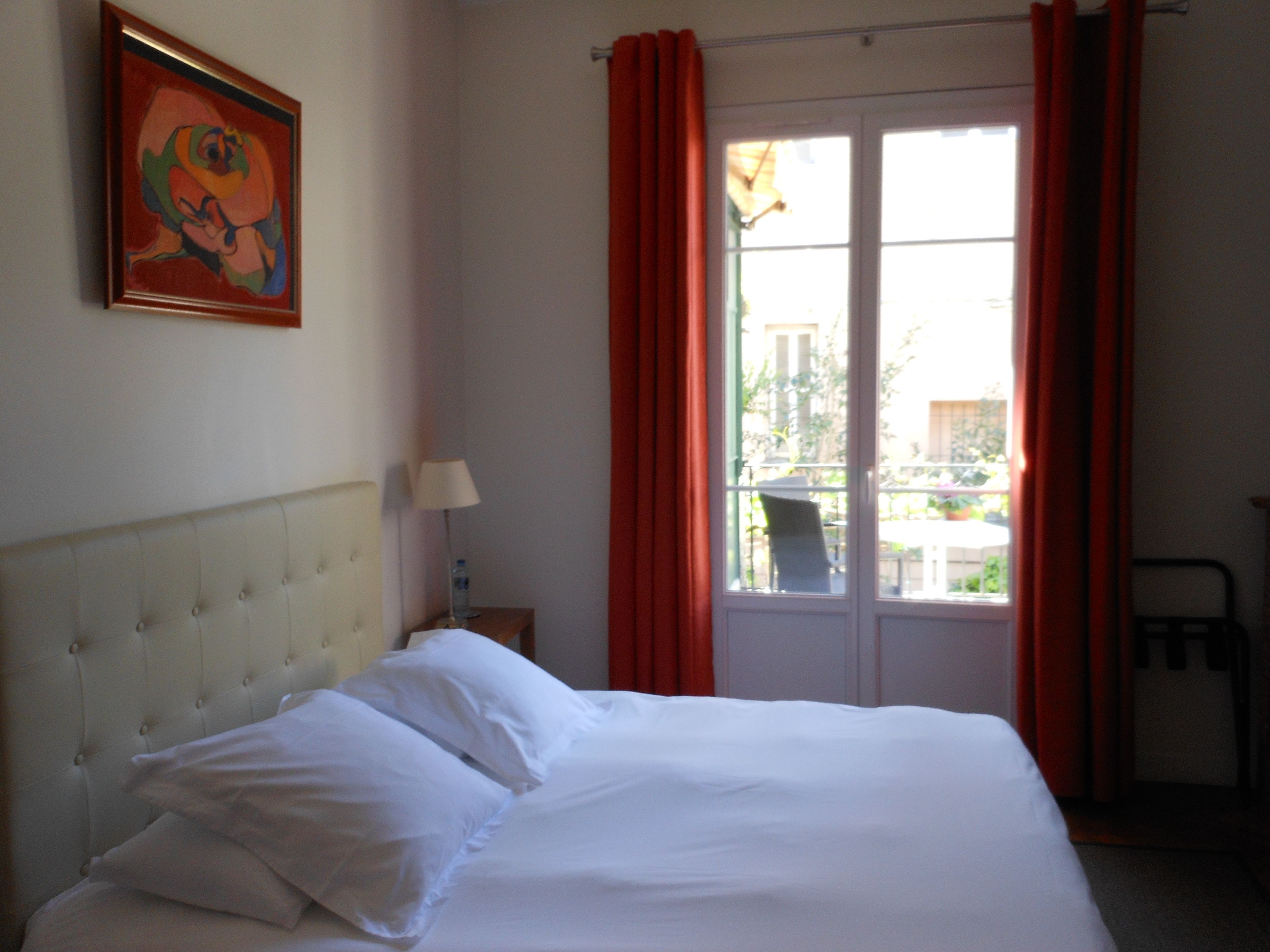 A hotel room with a bed, a nightstand, a lamp, and a window with curtains.