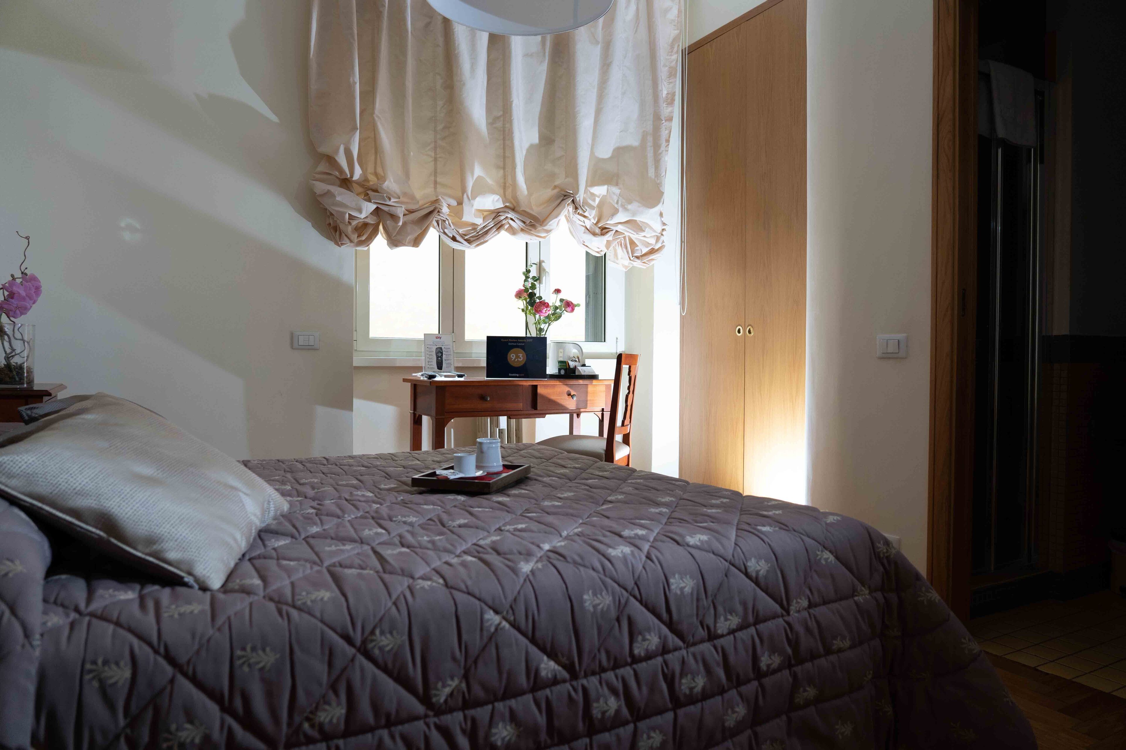 A bedroom with a bed, a desk, and a window with curtains.