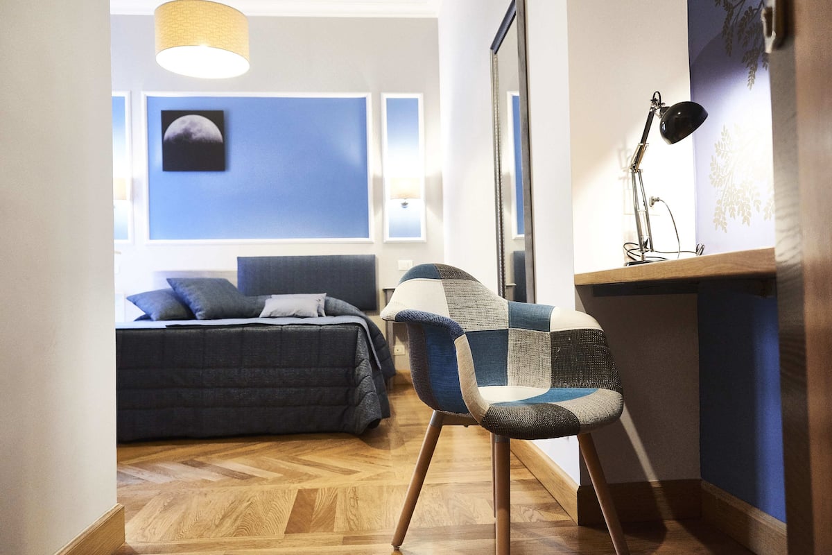 A bedroom with a bed, a chair, and a desk with a lamp.