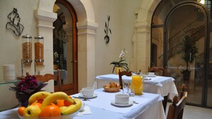 Colazione servita con frutta, caffè e succo su un tavolo in una stanza con archi e vista su una scalinata.