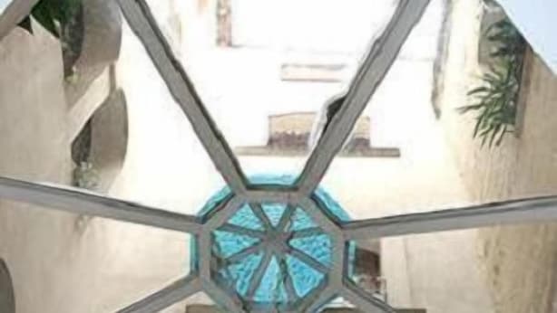 Una stanza con un design geometrico al soffitto, una cupola centrale e vista su un cortile esterno.