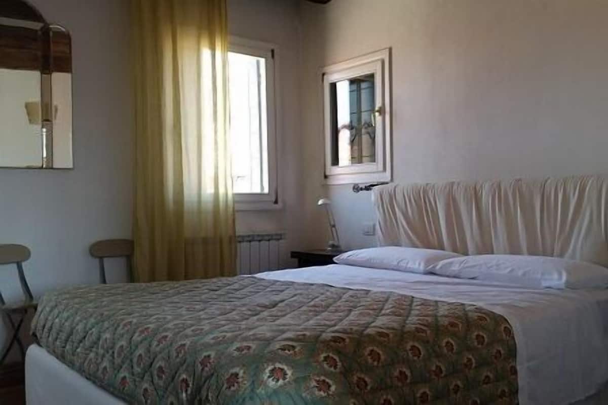 A bedroom with a bed, a window with curtains, a radiator, and a mirror on the wall.