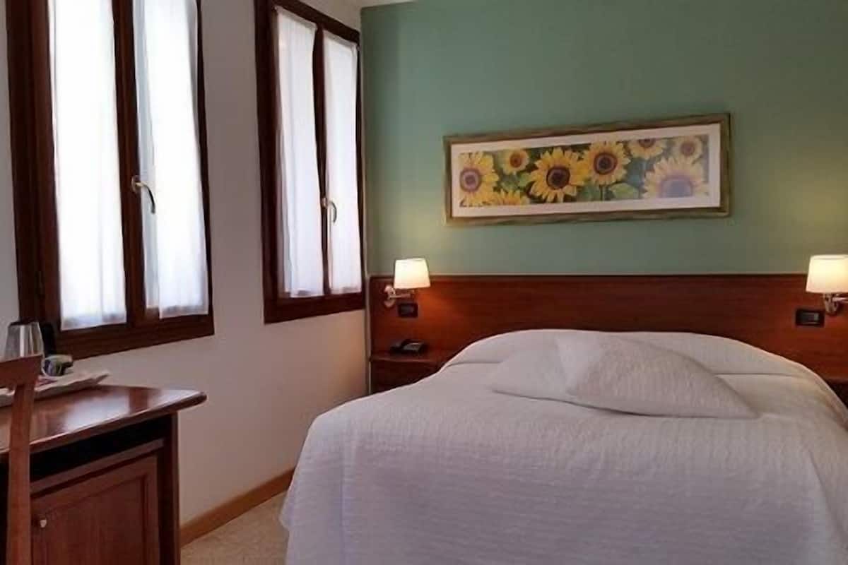 A hotel room with a bed, a desk, two bedside lamps, and a painting of sunflowers on the wall.