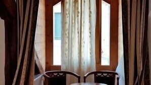 Ein gemütliches Zimmer mit Holzbalkendecke, zwei Stühlen, einem kleinen Tisch und einem Fenster mit Vorhängen.