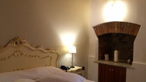 Ein Schlafzimmer mit Bett, Nachttisch, Lampe und einem Kamin aus Stein.