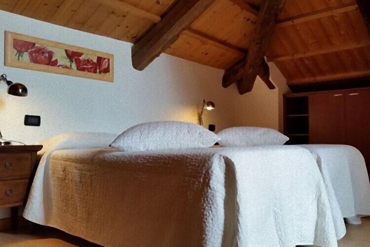 A bedroom with two beds, a wooden ceiling, a painting on the wall, and a nightstand with a lamp.