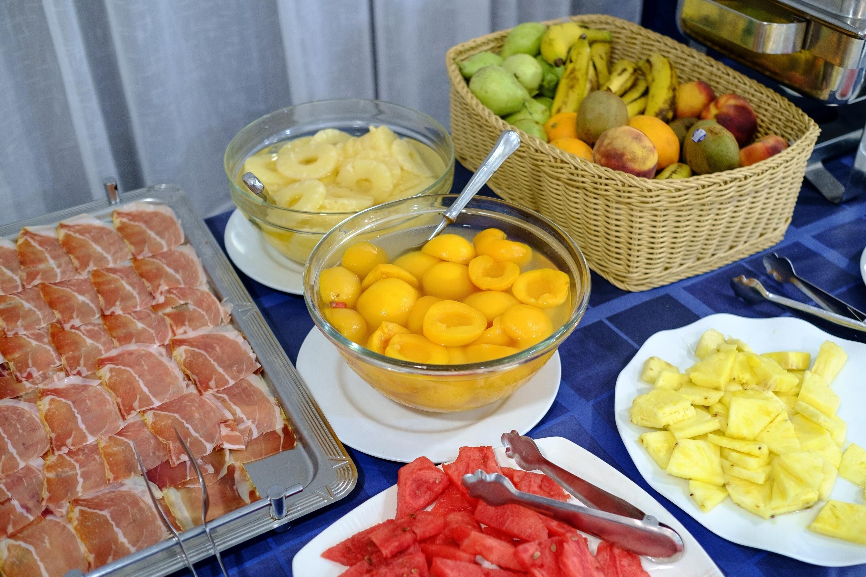 Ein reichhaltiges Buffet mit verschiedenen Speisen, darunter Aufschnitt, gelbe Früchte und ein Obstkorb.