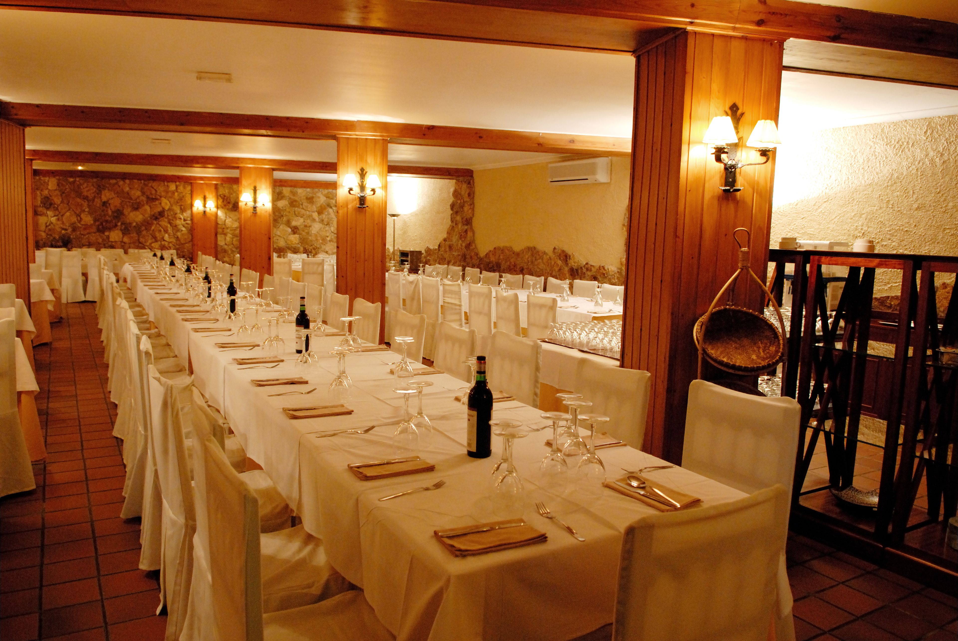 Un salón de banquetes con largas mesas dispuestas para comer, vigas de madera en el techo y paredes de piedra.