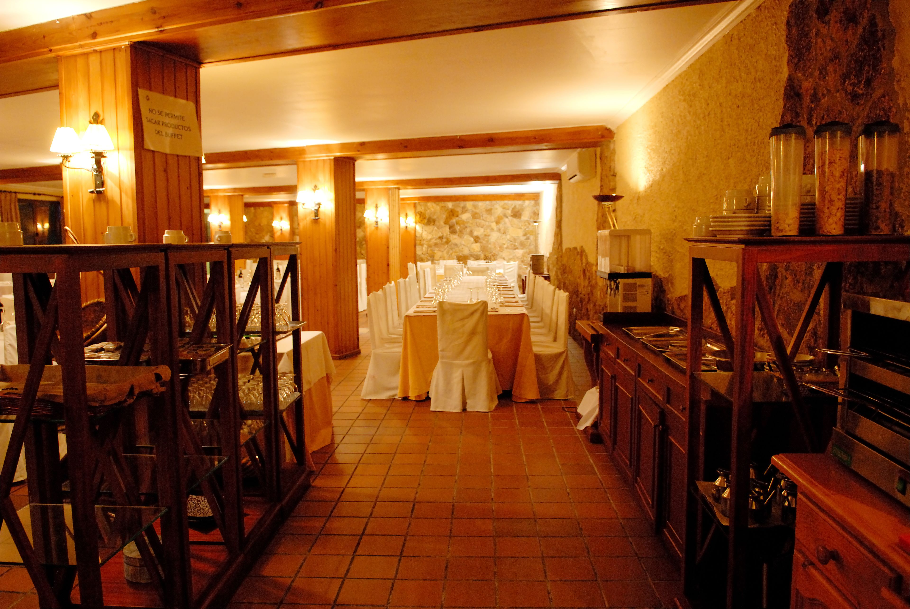 A restaurant with a long table set for a meal, wooden furniture, and a stone wall.
