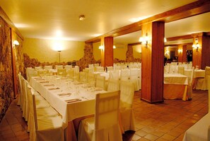 Un salón de banquetes con varias mesas redondas dispuestas para comer, con manteles blancos y sillas.